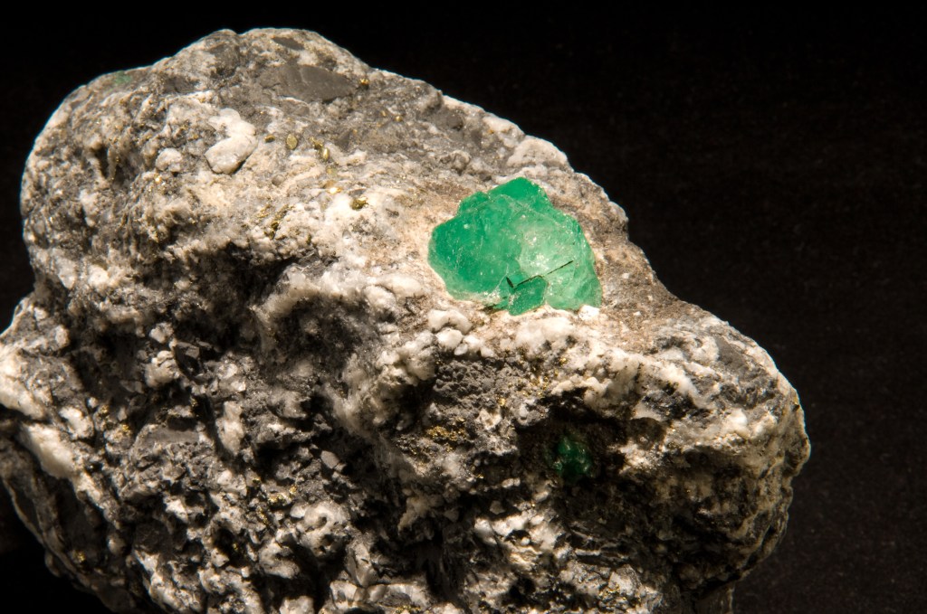 Close-up of a grey rock with green crystal formations embedded in it.