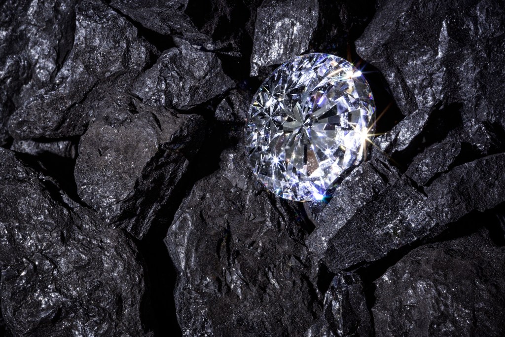 A sparkling diamond resting on a bed of coal, showcasing a contrast between luxury and raw material.